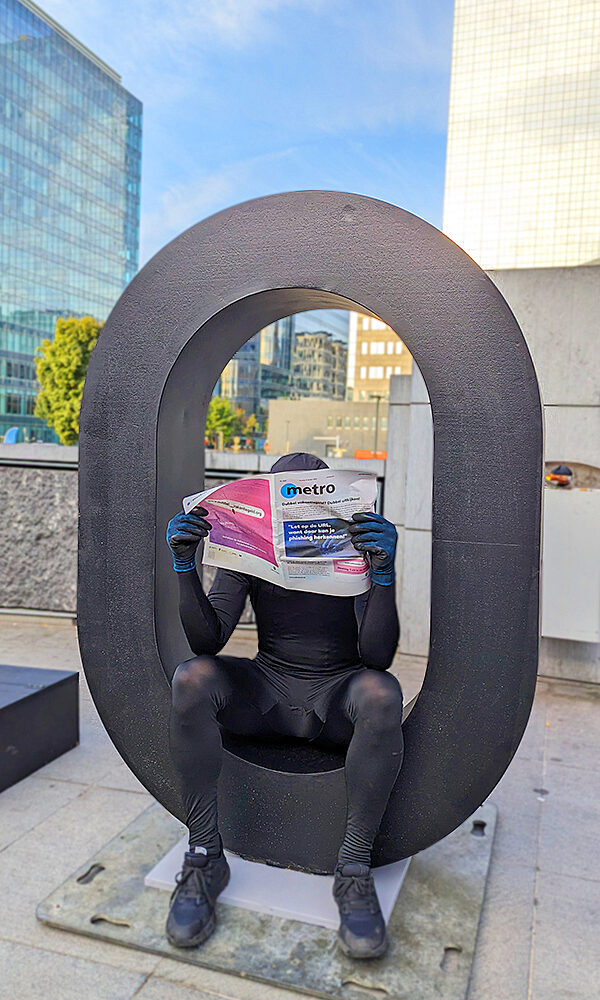 A person dressed in black reading the Metro newspaper, sitting inside a giant "O" from a public installation.
