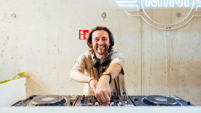 DJ souriant derrière ses platines, prêt à animer l’événement dans une ambiance détendue.
