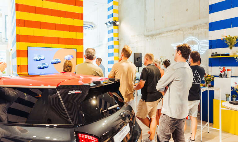 Groupe de visiteurs assistant à une présentation des modèles MINI à l’intérieur d’un showroom coloré.