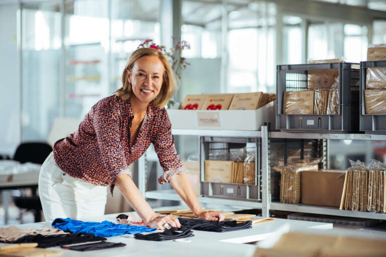 A female entrepreneur in a clothing workshop, surrounded by textile products and packaging.