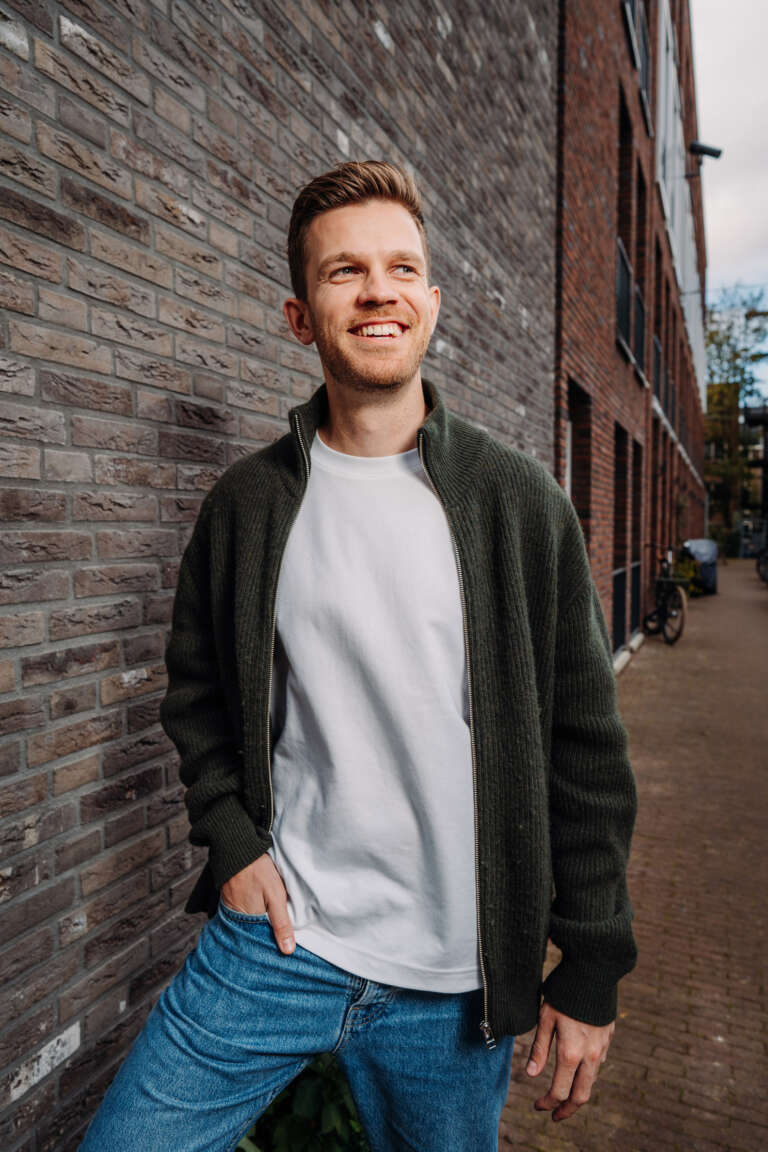 Portrait of a smiling young man outdoors, leaning against a brick wall.
