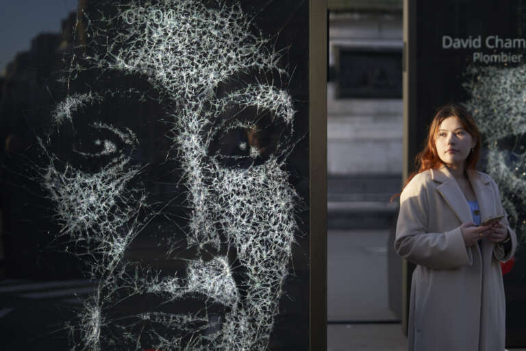 Femme passant devant un affichage artistique percutant représentant un visage fracturé