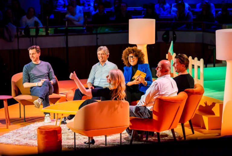 Table ronde sur scène dans un décor chaleureux et immersif, avec des intervenants en discussion devant un public